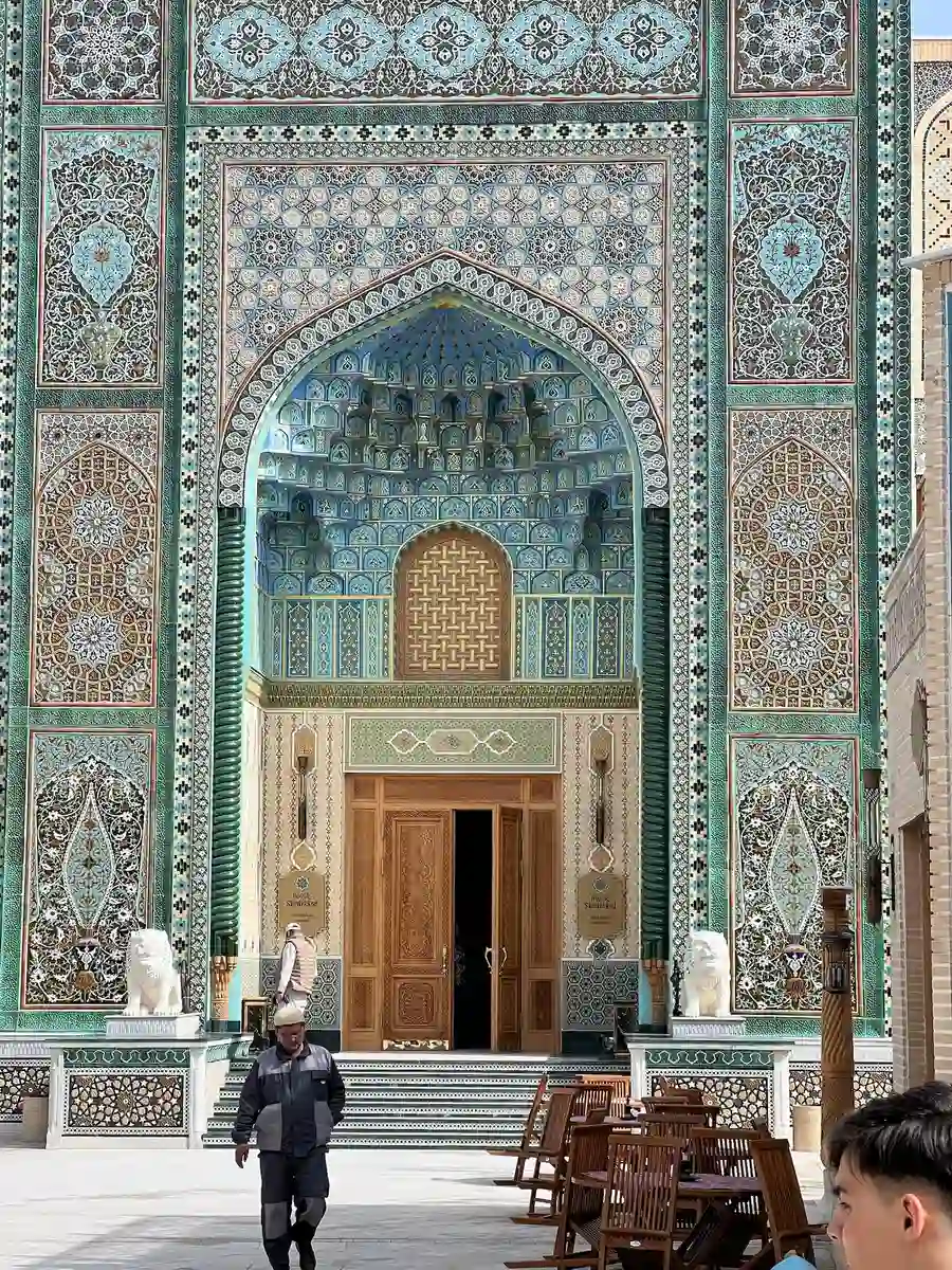 Ornately tiled entrance portal at Registan Square in Samarkand with people walking in the courtyard